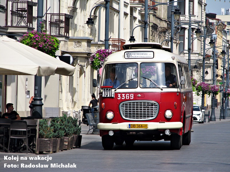 Zabytkowy, czerwono-biały autobus Jelcz 043, popularnie zwany „ogórkiem”, zaparkowany na brukowanej ulicy Piotrkowskiej w Łodzi w słoneczny, letni dzień. W tle widoczne ozdobne łódzkie kamienice i ogródki restauracyjne pod parasolami.