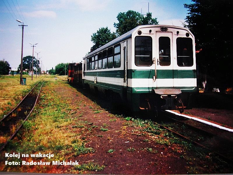 Historyczne zdjęcie z 2000 roku przedstawiające pociąg osobowy Kolei Rogowskiej na stacji Rawa Mazowiecka. Lokomotywa spalinowa Lxd2 z wagonami pasażerskimi stoi przy peronie starego dworca.