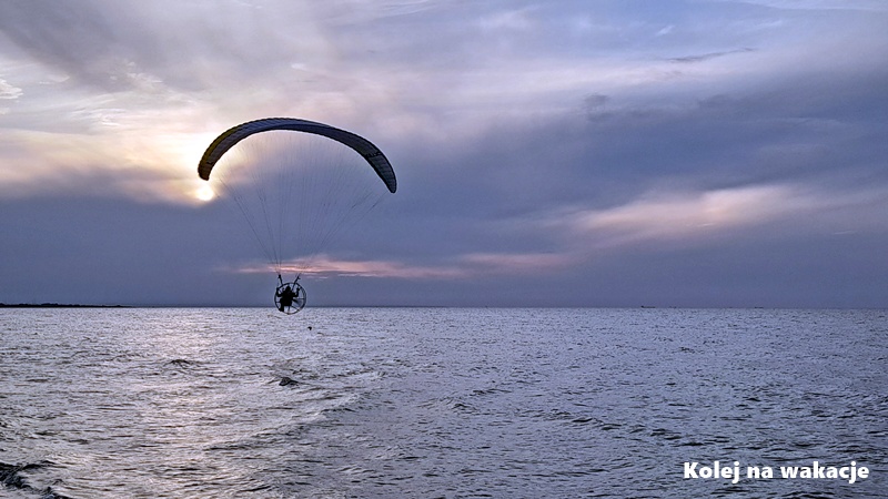 Paralotnia unosząca się nad plażą w Jantarze na tle przygaszonego, zamglonego zachodu słońca w chłodnych tonacjach.