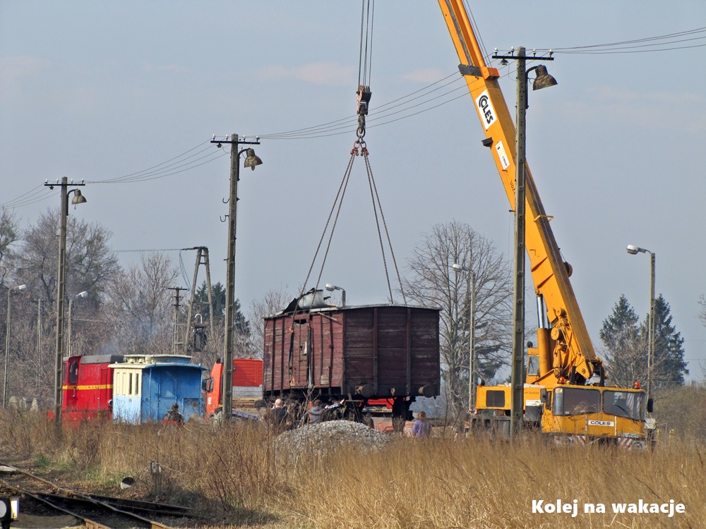Zdjęcie dokumentujące rozładunek zabytkowych wagonów wąskotorowych na stacji w Rogowie. Ciężki sprzęt zdejmuje uratowany przed złomowaniem wagon z platformy samochodowej na tory.