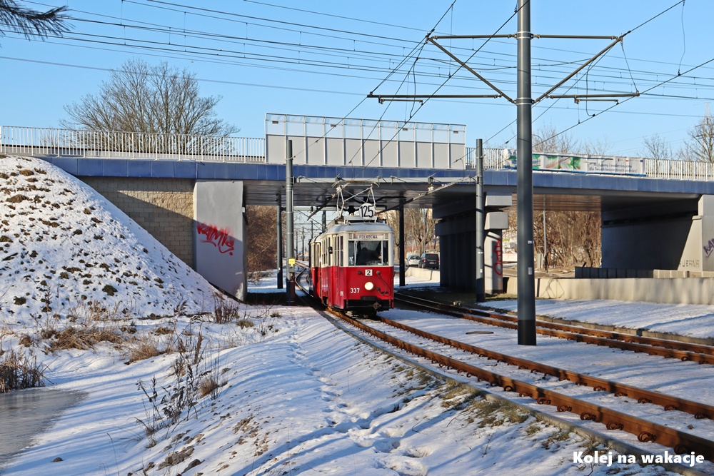 Zabytkowy czerwony tramwaj Konstal 5N z doczepą 5ND przejeżdża pod stalowym wiaduktem kolejowym w Zgierzu. Zimowa sceneria.