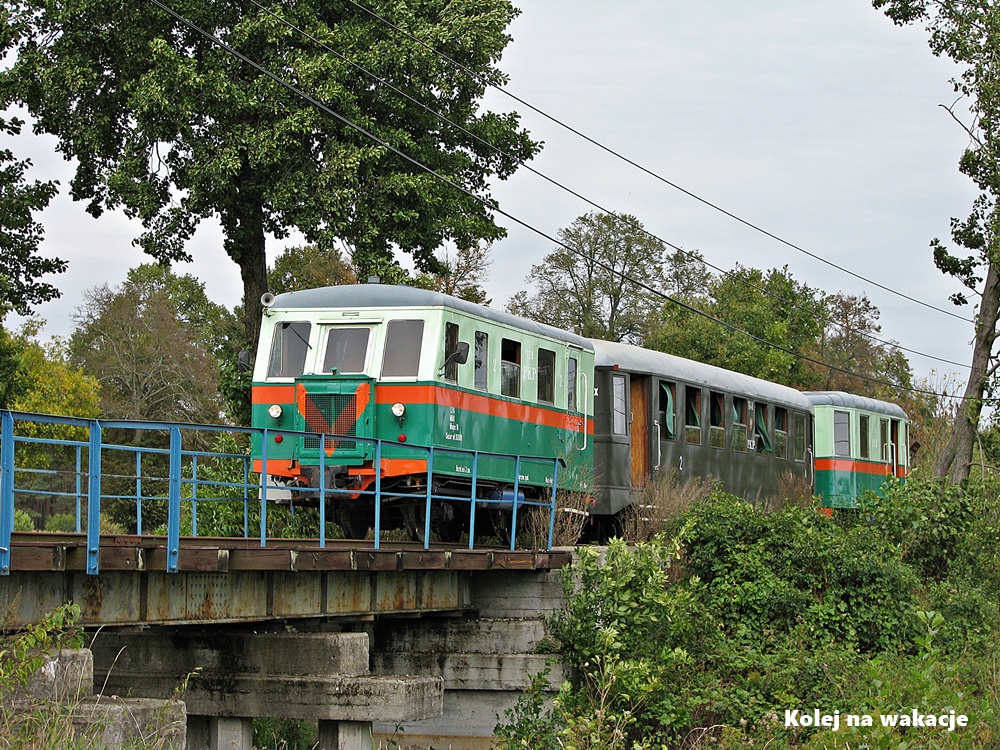 Sochaczewska Kolej Muzealna: Unikalny pociąg wąskotorowy złożony z dwóch wagonów motorowych MBd1 na końcach oraz wagonu pasażerskiego Bxhpi w środku na moście nad rzeką Łasica.