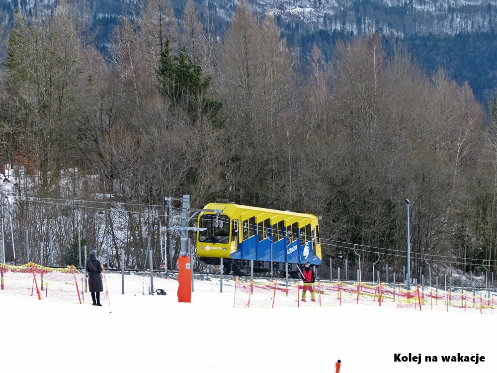 Kolej linowo-terenowa na Górę Żar zimą, wagon na trasie obok wyciągu narciarskiego na ośnieżonym zboczu.