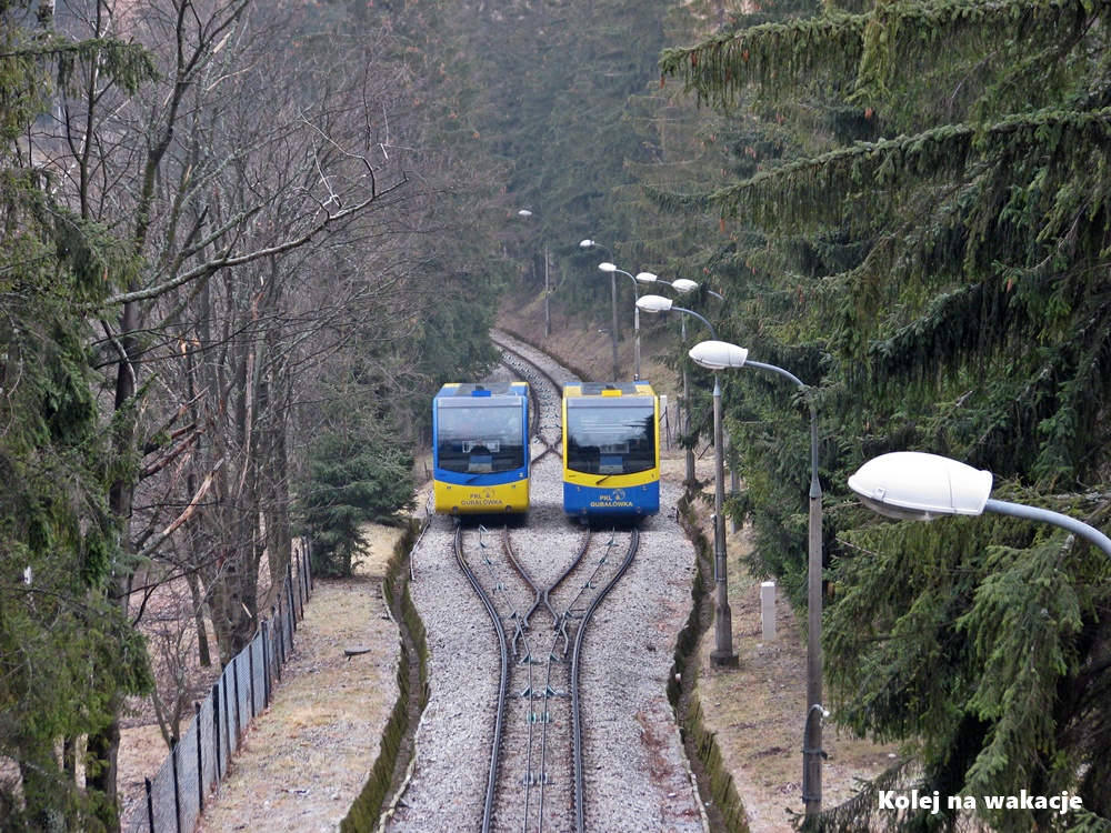 Kolej na Gubałówkę zimą – mijanka wagonów na tle zbocza Tatr.