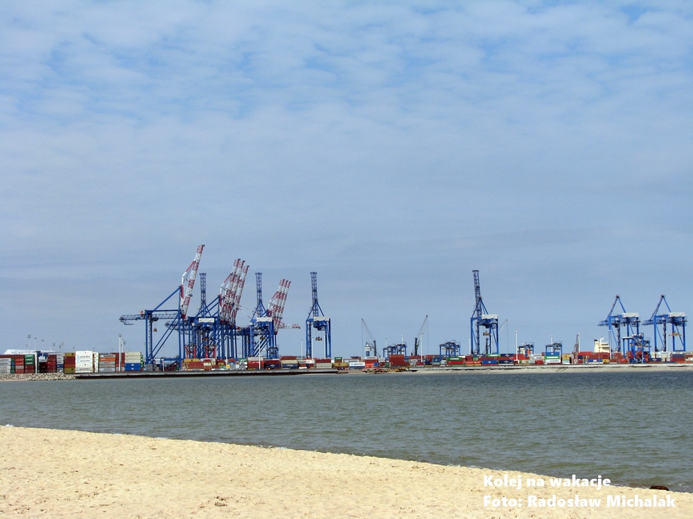 Widok z piaszczystej plaży na Stogach w stronę Portu Gdańsk; w oddali sylwetki dźwigów portowych.