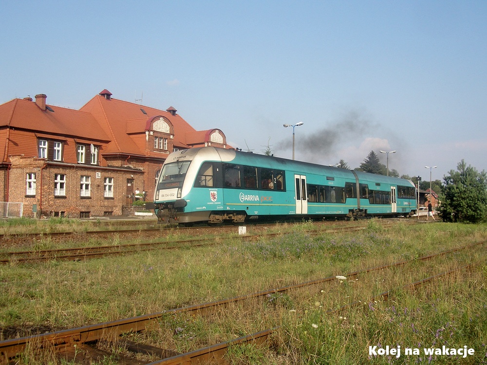 Szynobus Arriva SA134-002 odjeżdża ze stacji Tuchola w stronę Chojnic, w tle widoczny zabytkowy dworzec z czerwonej cegły.
