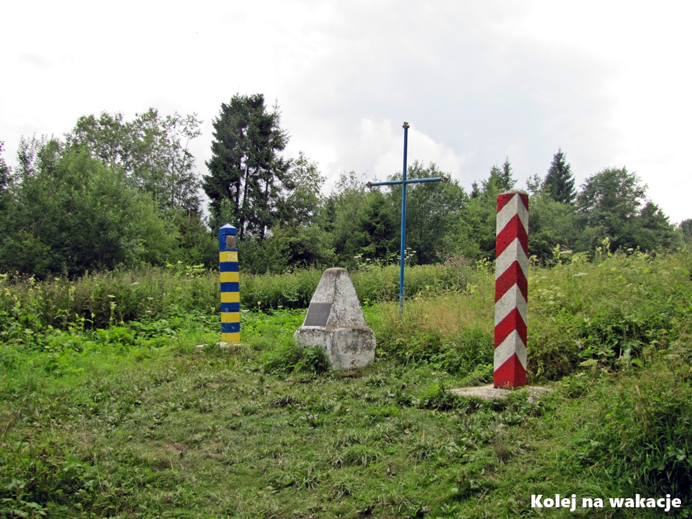 Symboliczne źródło rzeki San w Bieszczadach Zachodnich na granicy polsko-ukraińskiej. Po lewej stronie zdjęcia stoi niebiesko-żółty ukraiński słup graniczny, a po prawej biało-czerwony polski słup graniczny. Pomiędzy nimi znajduje się wysoki, metalowy krzyż pomalowany na niebiesko oraz tablica informacyjna z napisami w języku ukraińskim.