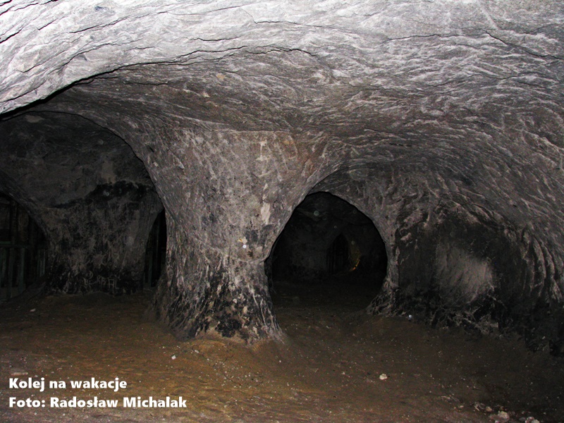 Wnętrze trasy turystycznej w Grotach Nagórzyckich w Tomaszowie Mazowieckim. Podziemne wyrobiska z widocznymi filarami z jasnego piaskowca, klimatycznie podświetlone sztucznym światłem.
