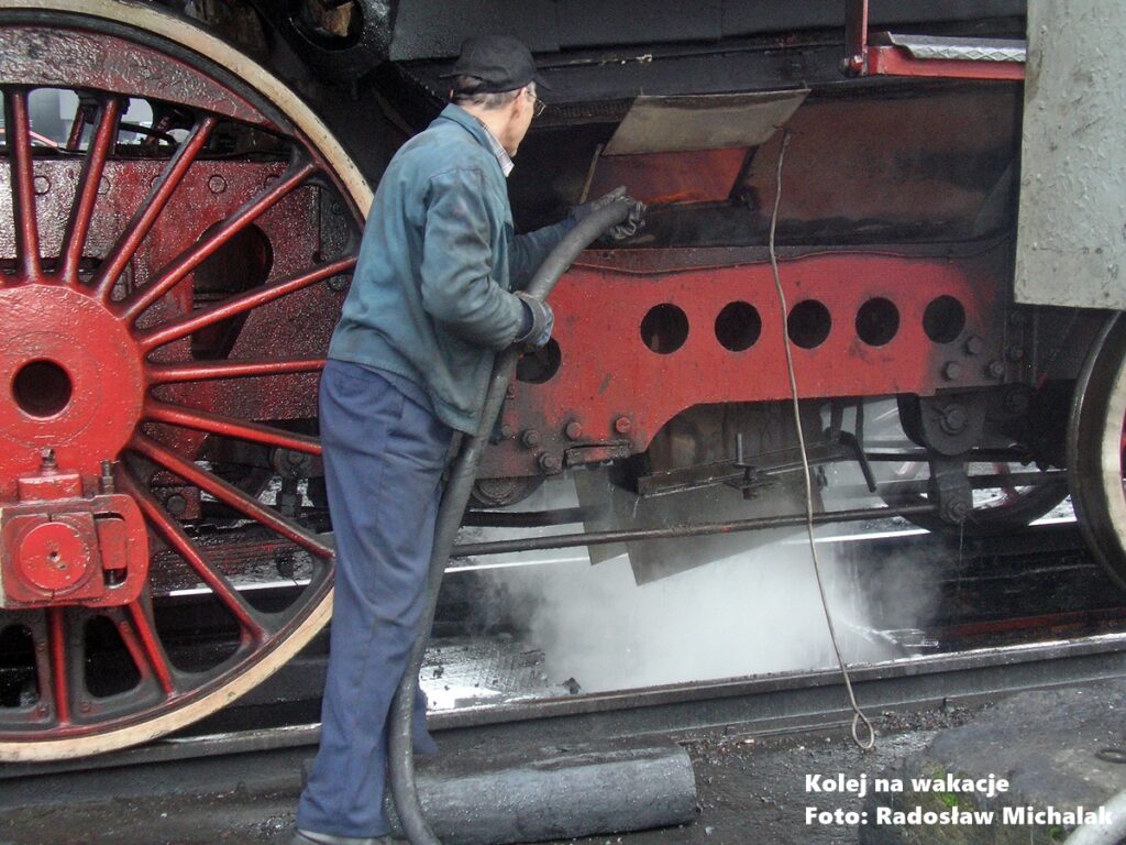 Pracownik Parowozowni Wolsztyn wykonujący przegląd techniczny czynnej lokomotywy parowej.