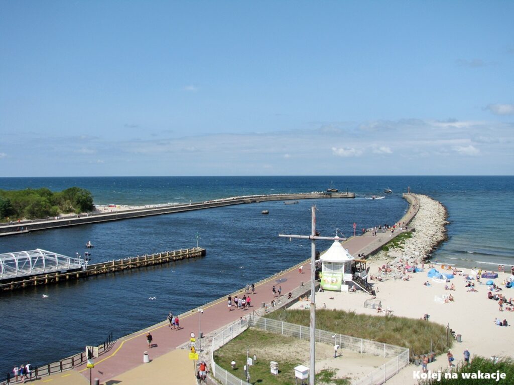 Widok z góry latarni morskiej w Ustce na wejście do portu, falochrony i otwarte Morze Bałtyckie.