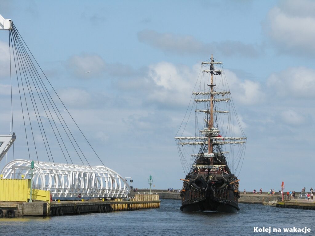 Most obrotowy dla pieszych w Ustce z napisem „USTKA” oraz statek turystyczny wpływający do portu.