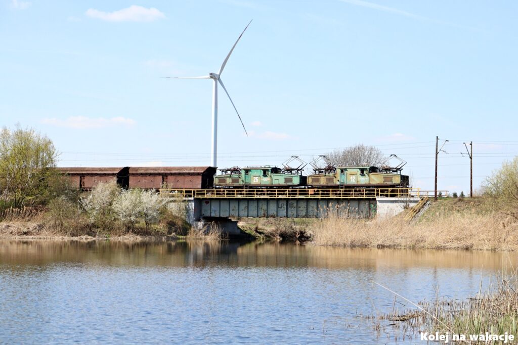 Dwa Krokodyle EL2 w trakcji podwójnej na moście w Wygodzie. W tle jezioro i turbina wiatrowa.