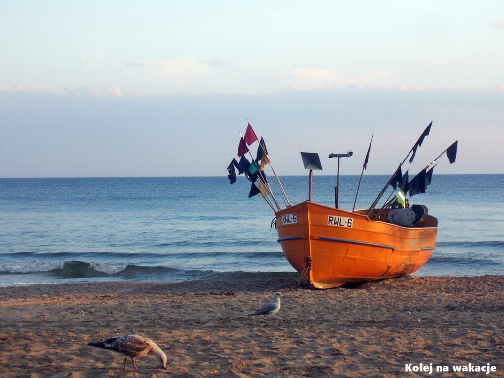 Spokojny poranek na piaszczystej plaży w Rewalu z wyciągniętą na brzeg tradycyjną łodzią rybacką.