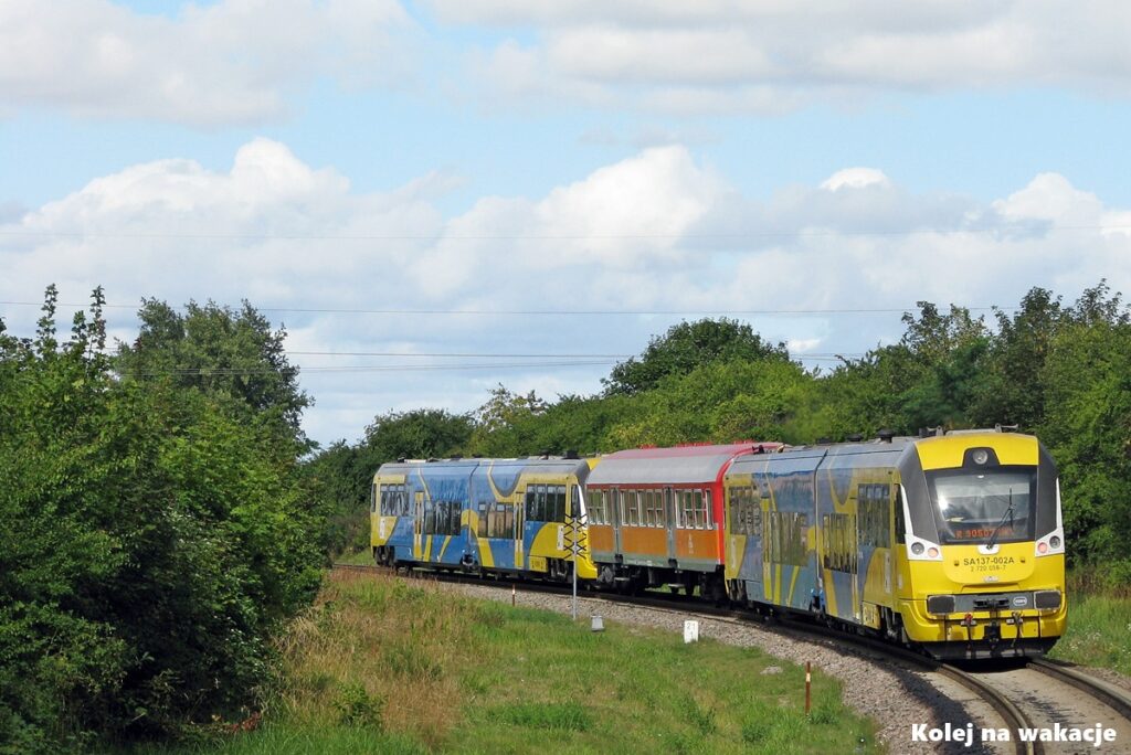 Szynobus SA137 z doczepionym klasycznym zielonym wagonem typu bonanza na lokalnej trasie kolejowej.