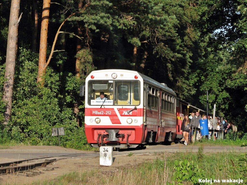 Pociąg Żuławskiej Kolei Dojazdowej z czerwoną lokomotywą MBxd2-212 na leśnej stacji Jantar Port.