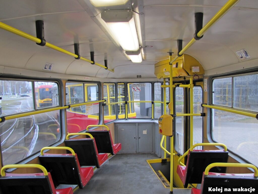 Wnętrze zabytkowego tramwaju 13N w Warszawie. Widok przez szybę wagonu doczepnego na pierwszy wagon składu oraz nowoczesny tramwaj Pesa w tle.