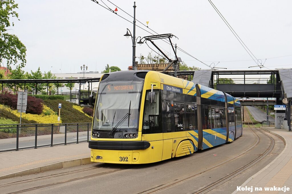 Żółto-niebieski tramwaj Pesa 122NbT Swing (linia nr 5) stojący na przystanku przy ulicy Traugutta, niedaleko dworca Toruń Miasto.