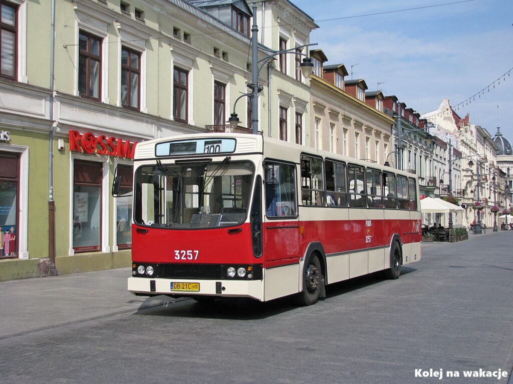 🚋 Jak zwiedzić Łódź tramwajem? Gotowy plan wycieczki po mieście 1 Zabytkowy czerwony autobus Jelcz linii turystycznej 100 na ulicy Piotrkowskiej w Łodzi na tle historycznych kamienic.