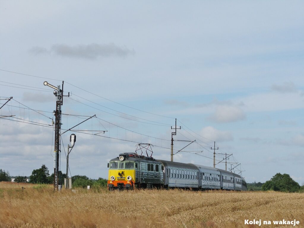 Pociąg pasażerski PKP Intercity prowadzony przez klasyczną lokomotywę EP07-442 mija zabytkowy semafor kształtowy. Skład jedzie przez złote, letnie pola w okolicach nadmorskiej miejscowości Sianożęty.